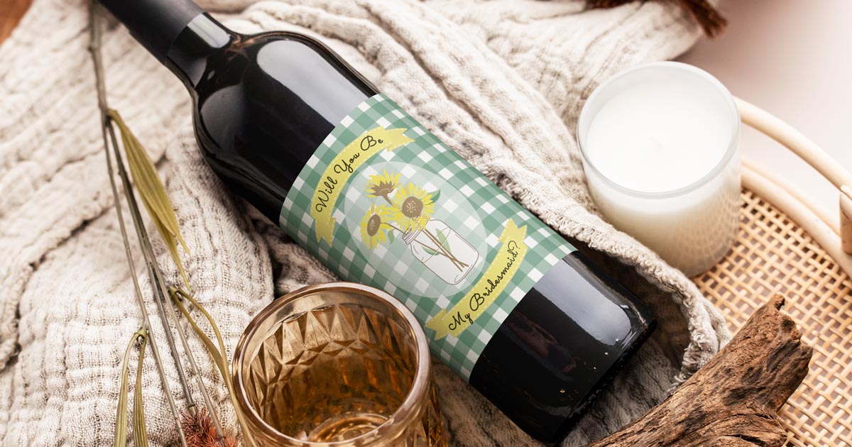 Wine bottle laying on a blanket and other gifts, with green checkered bridesmaid proposal label